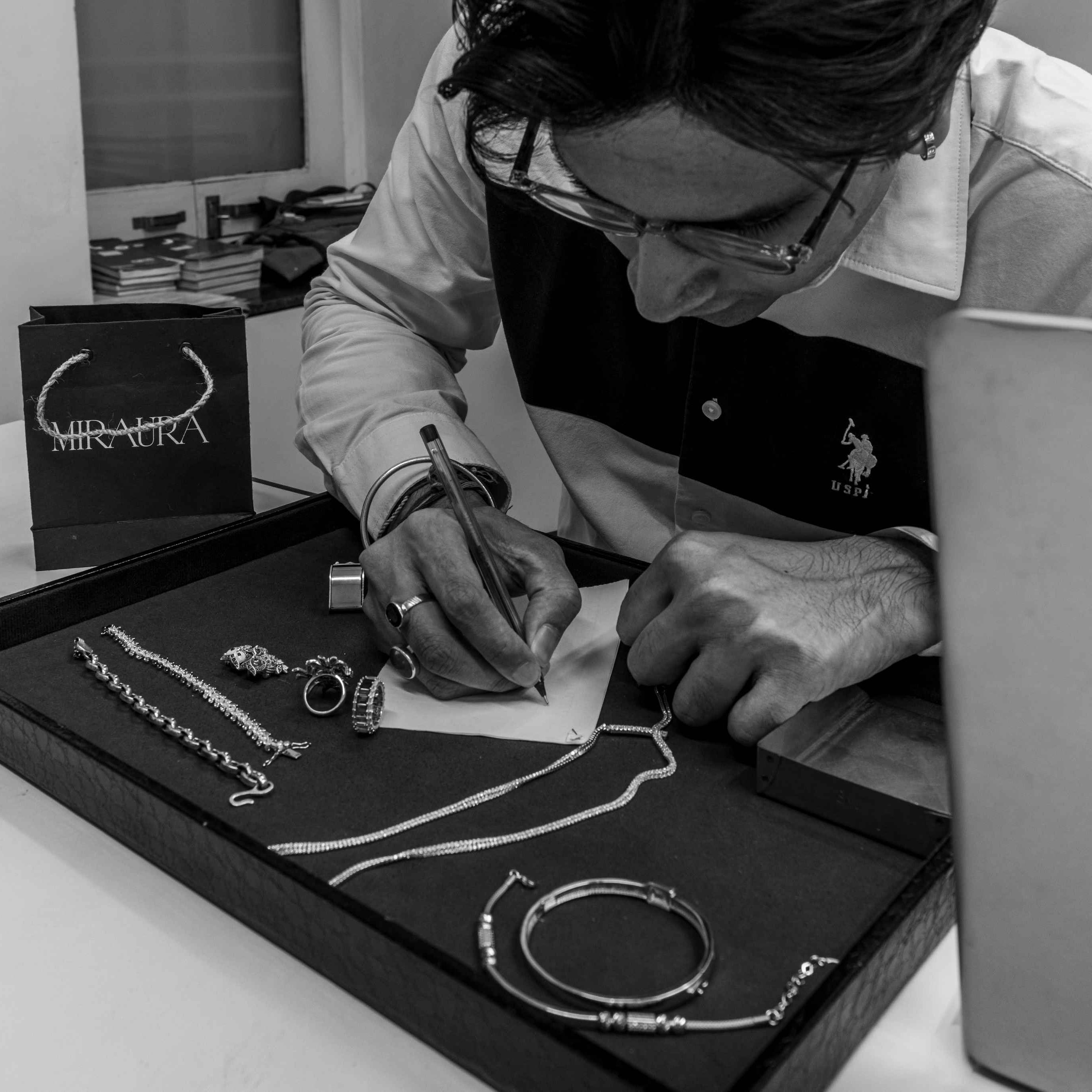 Founder of Miraura Jewels, Ratnesh Pansari working on jewelry designs with a laptop and jewelry display on a table.