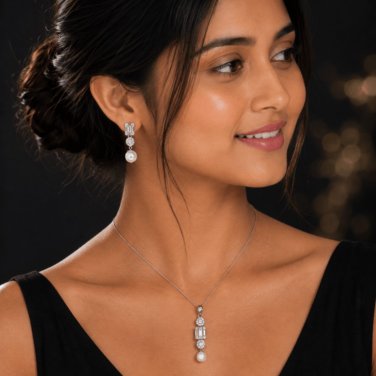 A woman wearing a Baguette Zirconia & Pearl Pendant Set silver drop  earring with clear gemstones and white pearl accents, shown against a dark blurred background. Miraura Jewels