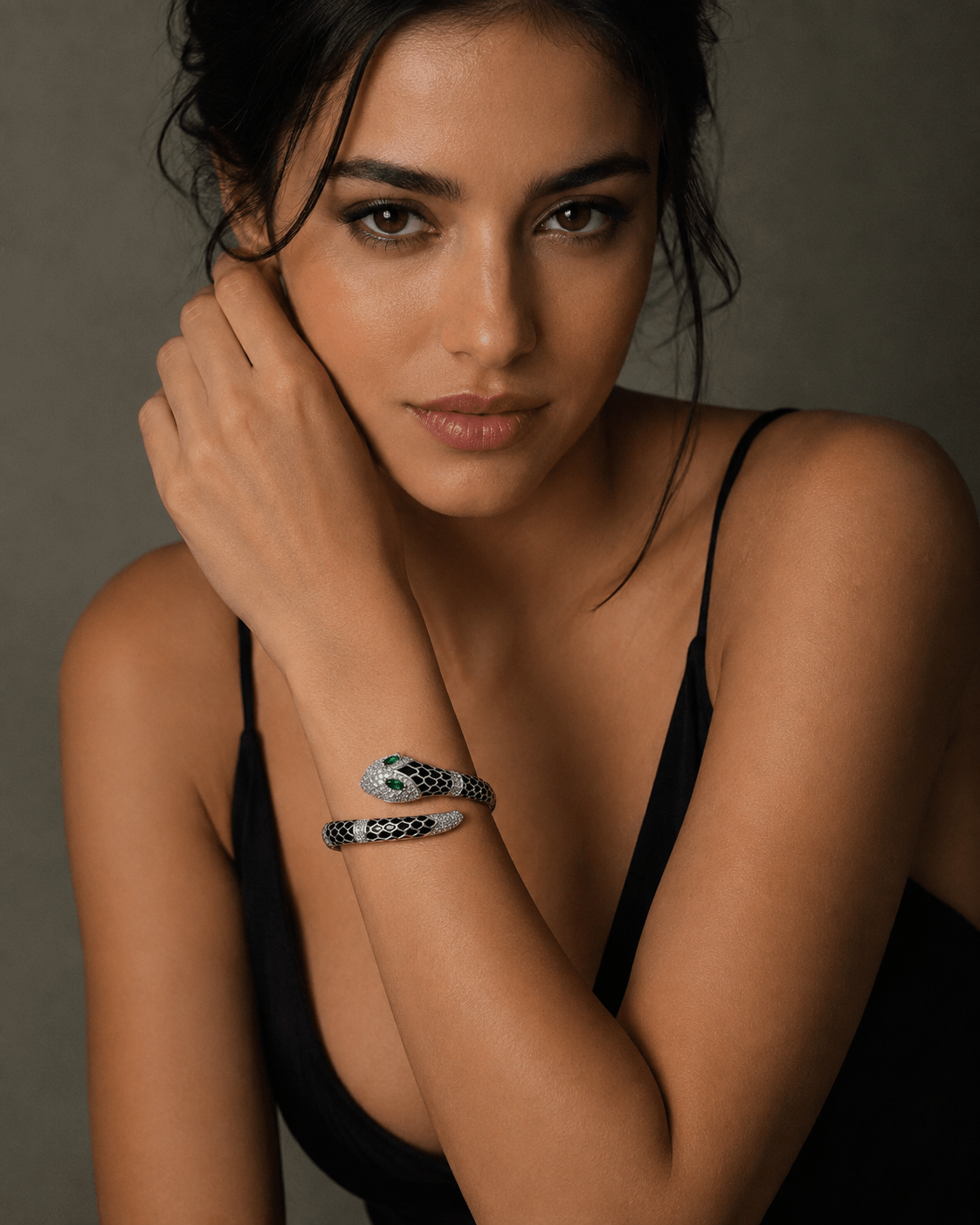 A close-up portrait of a woman wearing a black spaghetti-strap top and a black-and-white patterned snake cuff bracelet by miraura jewels on her wrist.
