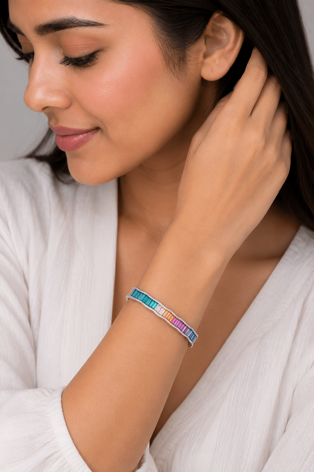 A woman wearing a slim silver-toned bangle bracelet with a vibrant rainbow-colored striped pattern, shown in a close-up lifestyle shot.