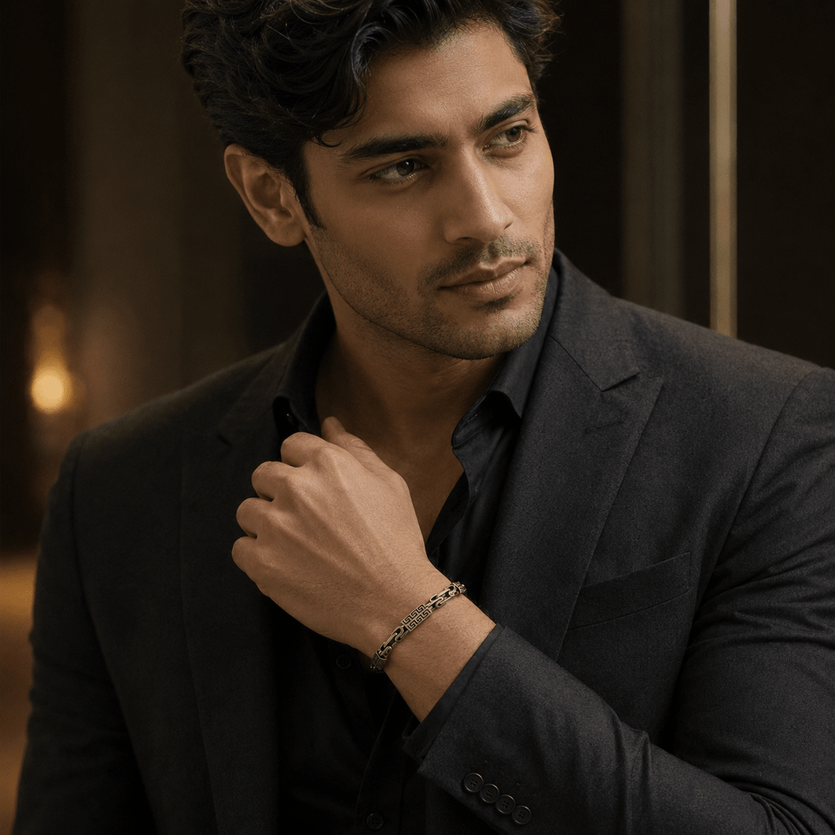 A man in a dark gray blazer and black shirt wearing a 925 Sterling Silver Oxidised Greek Key Link Bracelet by Miraura Jewels.