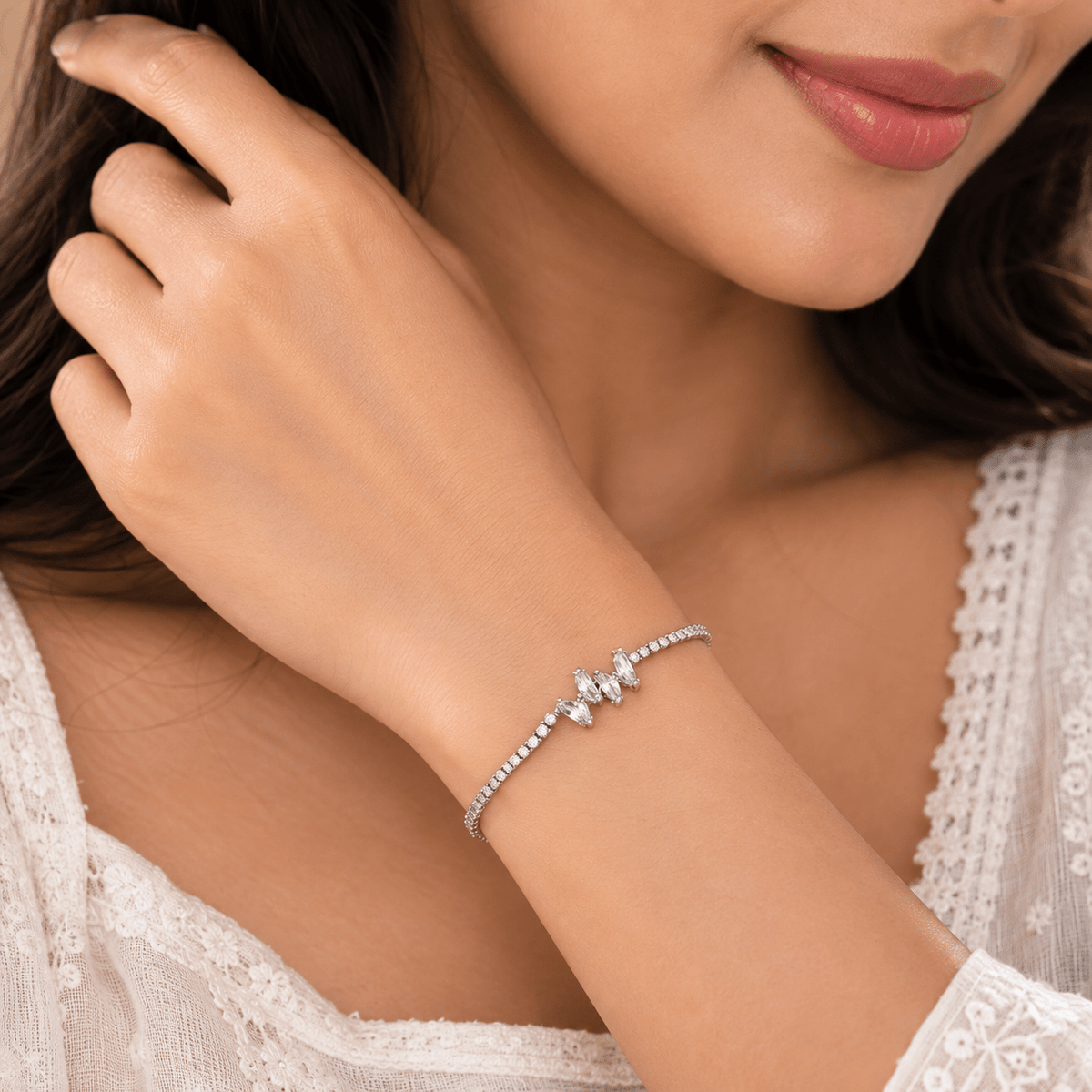 A close-up lifestyle shot of a woman wearing a delicate silver-toned bracelet with a central butterfly design set with clear stones. The image shows her hand resting near her face, wearing a white lace top.
