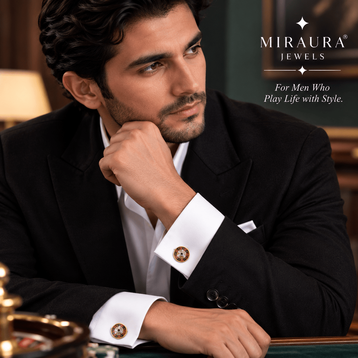 A man in a black suit and white dress shirt wearing gold Miraura Jewels cufflinks, posed in a luxurious indoor setting with the brand logo in the top right corner.