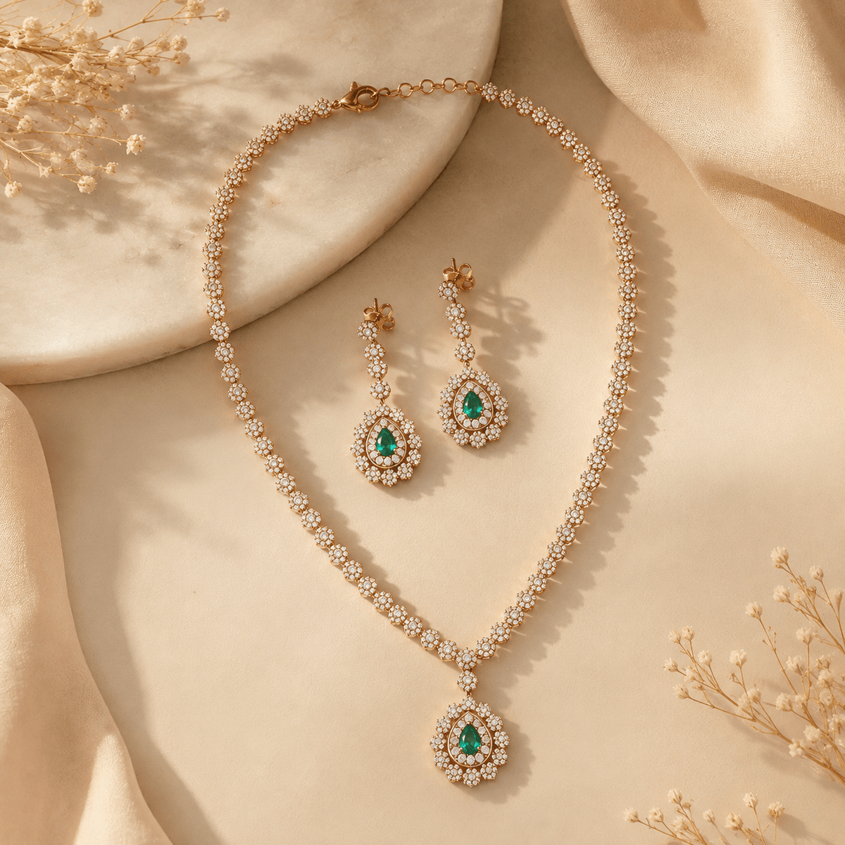 Gold jewelry set with a necklace and matching drop earrings, featuring green teardrop gemstones.