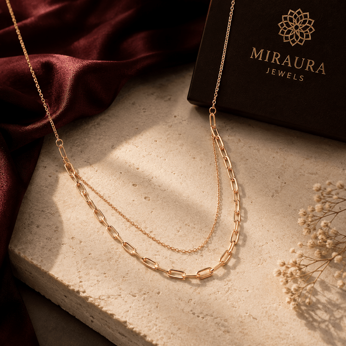 A 925 Silver Double-Layered Rose Gold Link Chain displayed on a textured stone slab next to a dark brown Miraura Jewels box and draped burgundy fabric.