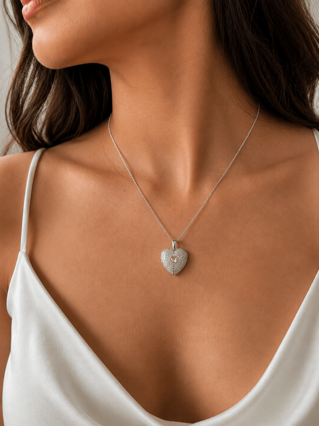 A close-up of a woman wearing a delicate Miraura Pave Crystal Open Split Heart Pendant with a pink center, styled with a white camisole.