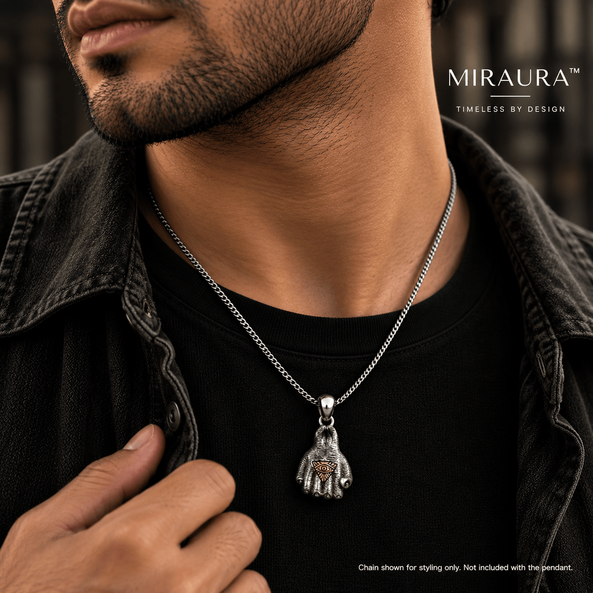 A close-up lifestyle shot of a man wearing a silver chain with a detailed fist with illuminati insignia pendant. 