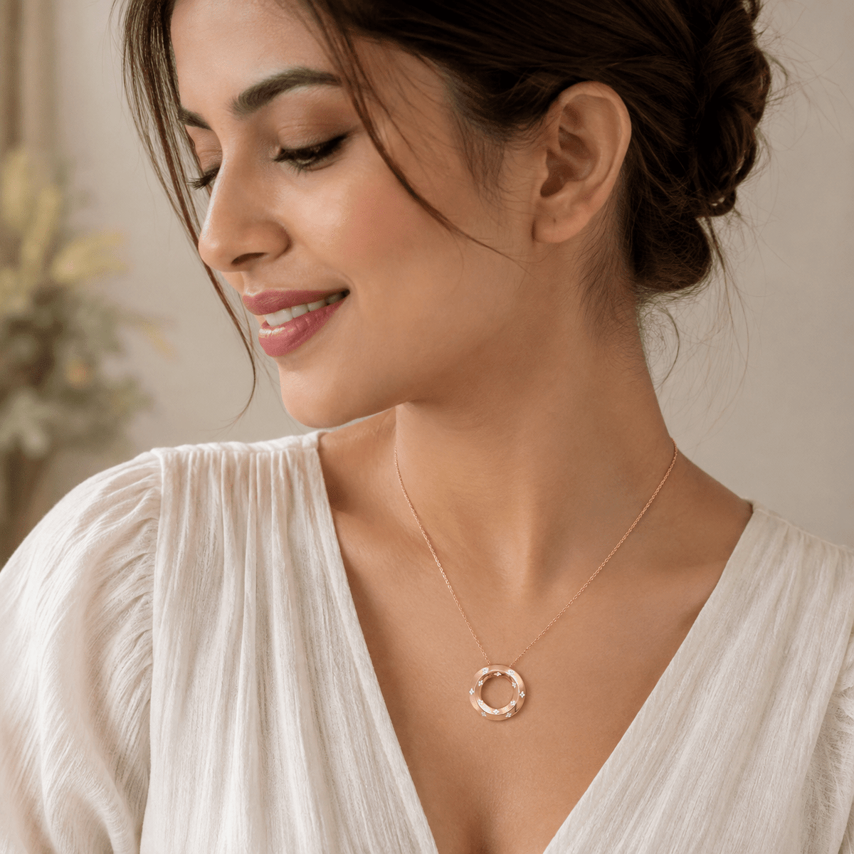 A woman wearing a delicate Miraura's Rose Gold Segment Pendant, styled with a cream-colored blouse against a soft, warm neutral background.