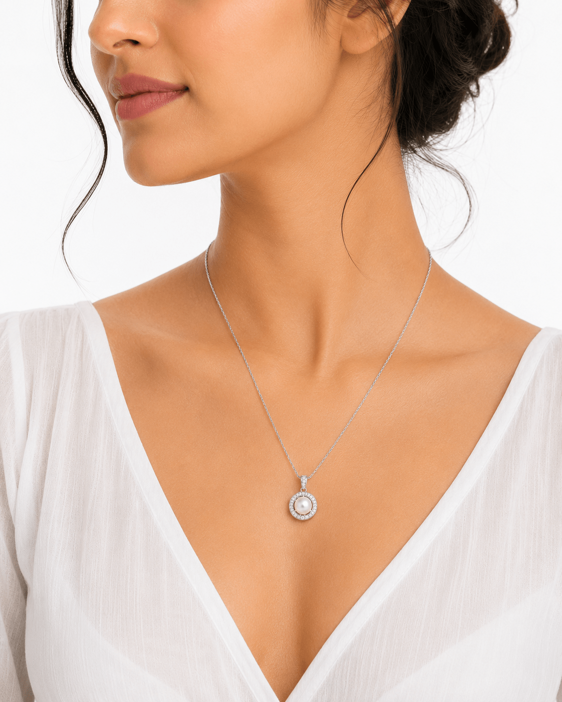 A close-up of a woman wearing a delicate Miraura Pearl & Sparkling Crystal Halo Silver Pendant with a round clear zirconia baguettes  surrounded by a pearl halo.