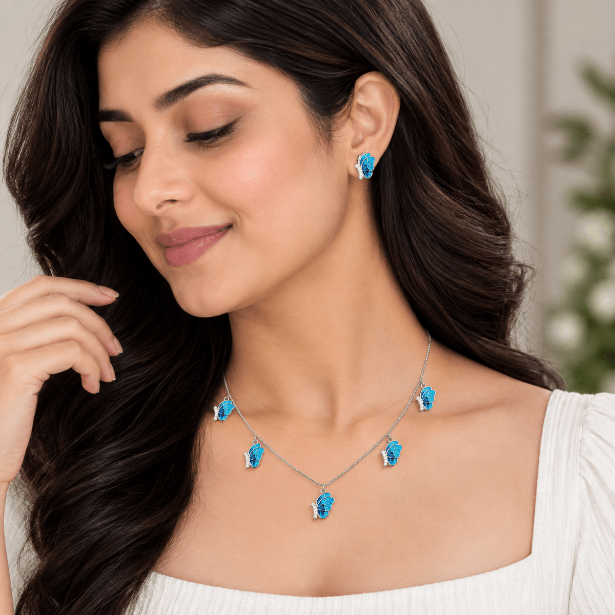 A woman wearing a matching jewelry set with a silver necklace and matching stud earrings, each featuring a bright blue teardrop-shaped crystal or gemstone, shown in a close-up portrait.