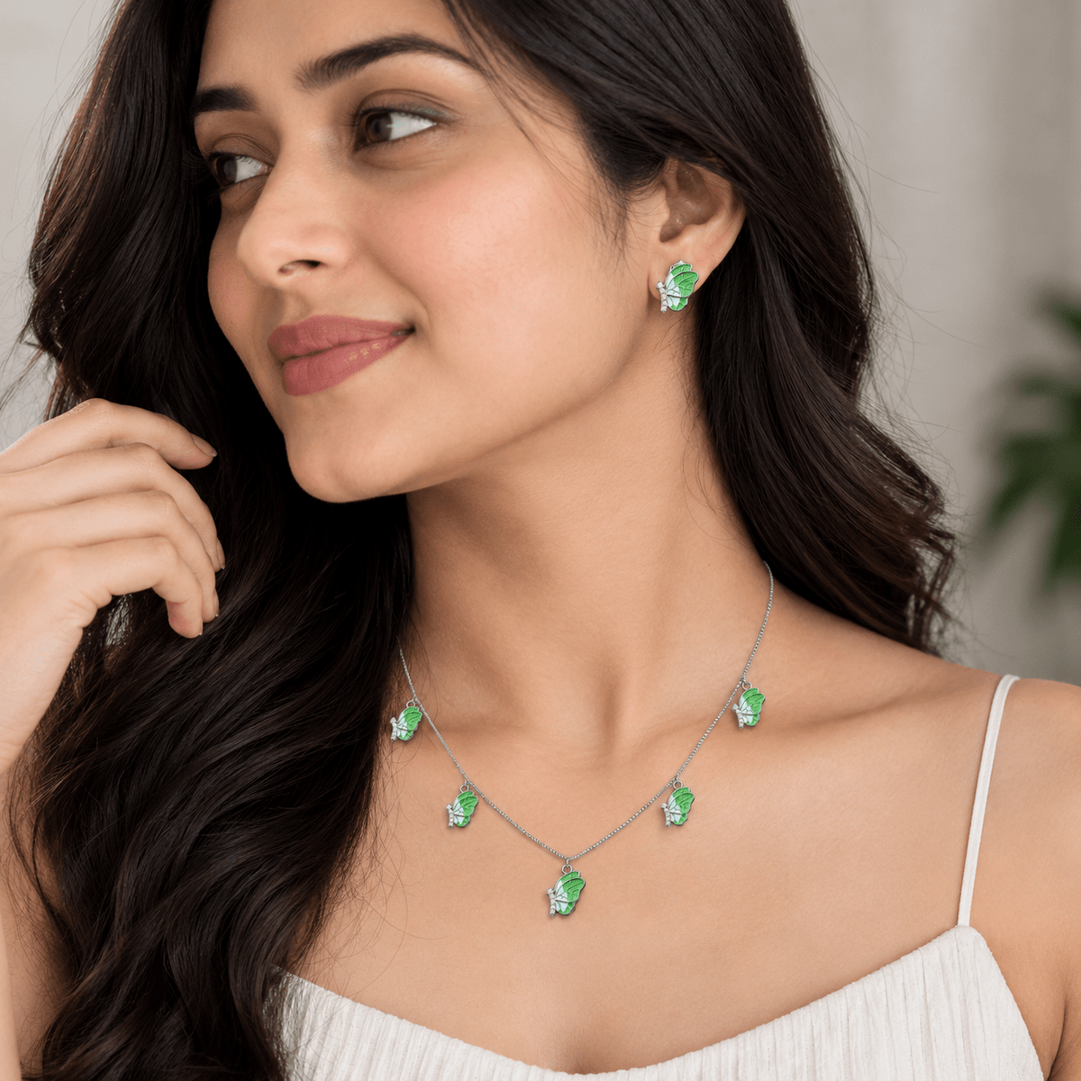A woman wearing Miraura's 925 silver necklace and matching stud earrings with bright green leaf-shaped stones, shown in a softly lit indoor setting.