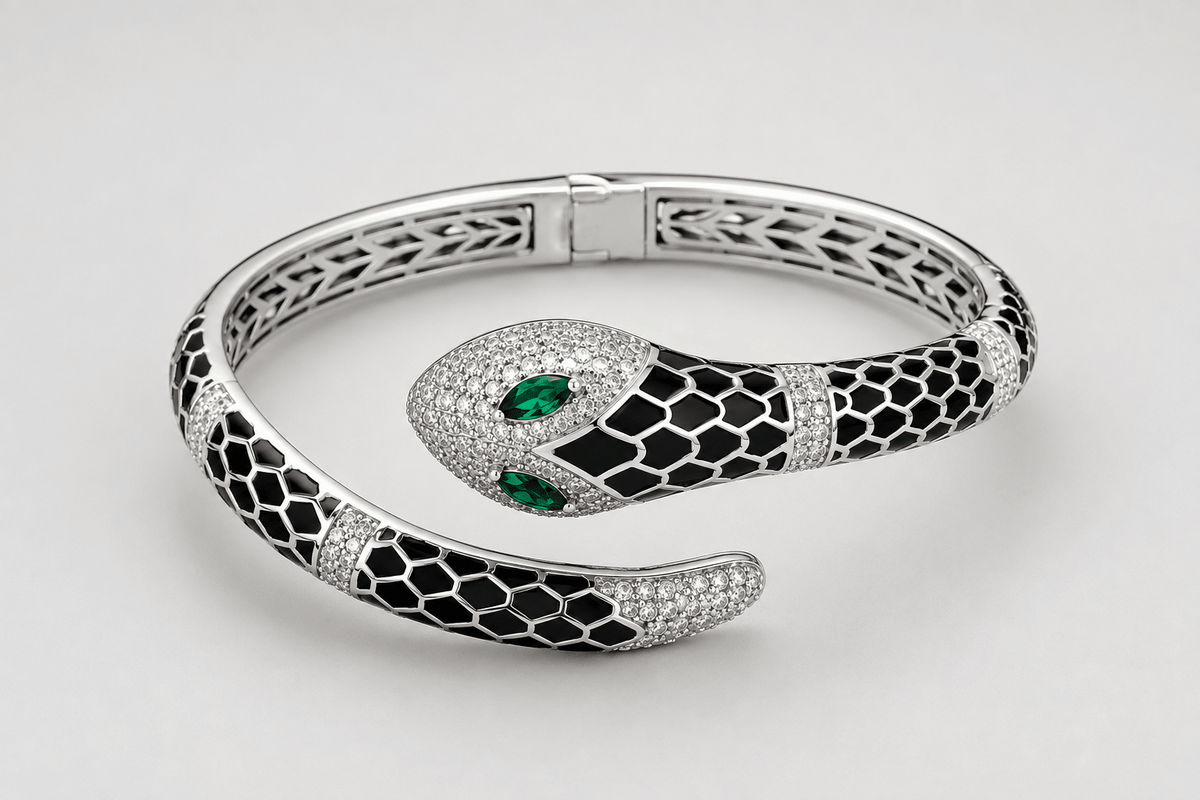 A 925 silver snake-shaped cuff bracelet featuring black enamel scales, pavé-set clear stones, and two green emerald-cut gemstones in the eyes by Miraura Jewels.