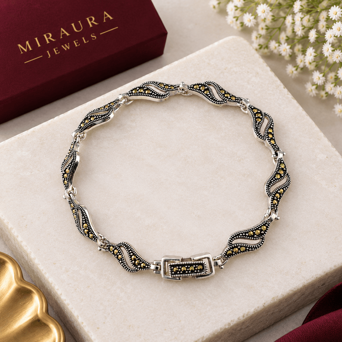 A Miraura Jewels, The Eternal Eye: 925 Silver Marquise Link Bracelet. A Oxidised silver-toned wavy bracelet with black and yellow stone accents, displayed on a cream-colored stone block with its branded box in the background.