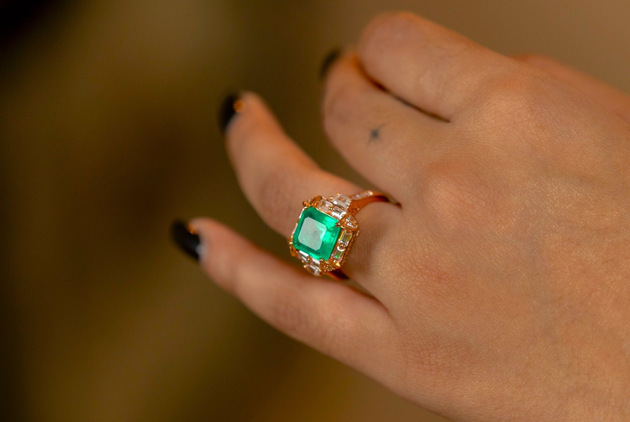 Hand wearing Miraura's Emerald Green Statement Ring with a blurred chandelier in the superbly lit background.