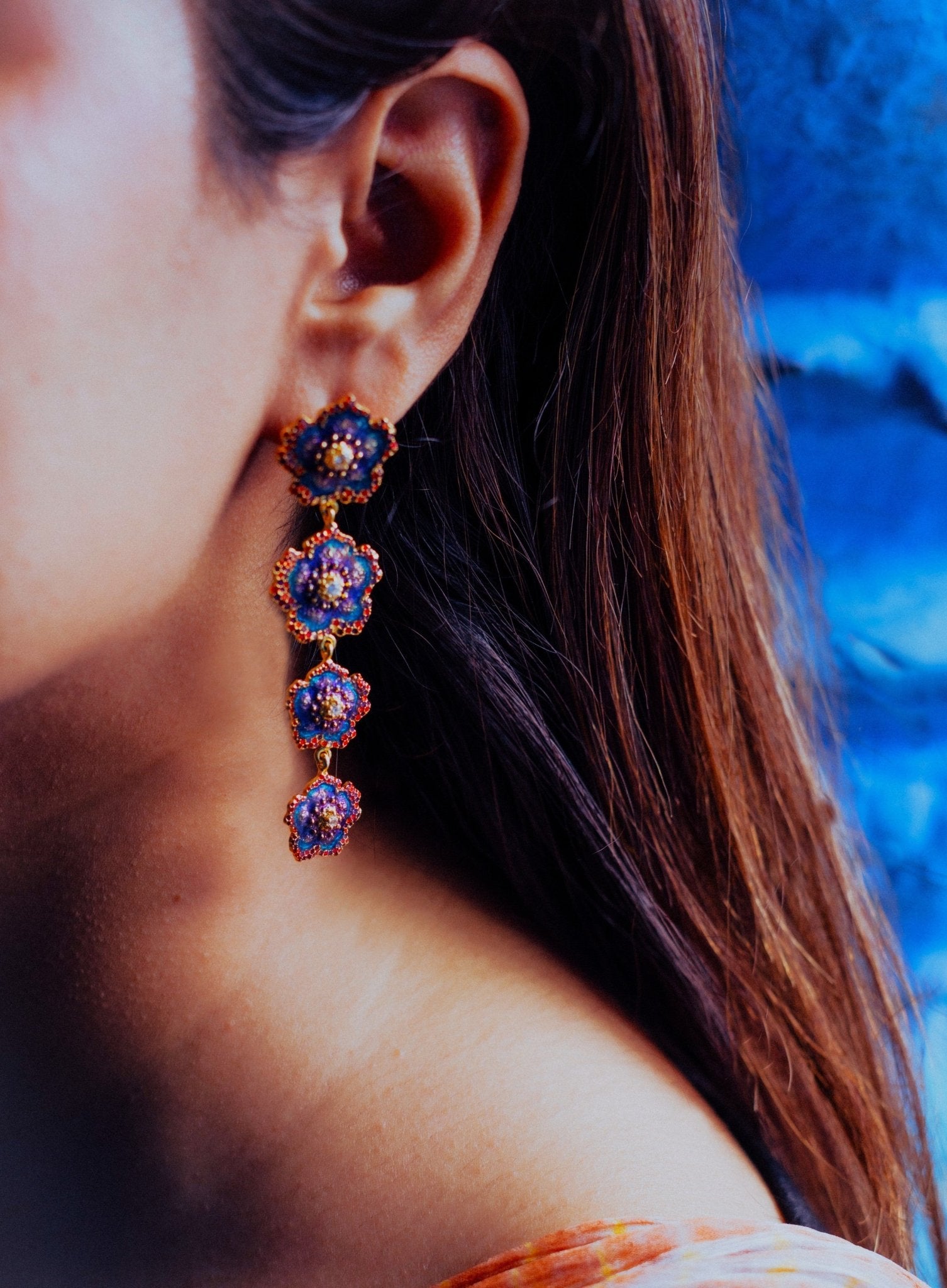 Close-up of a girl wearing a Enamel Floral Cascade Drop Earrings by Miraura Jewels with a blue jodhpur's backdrop.